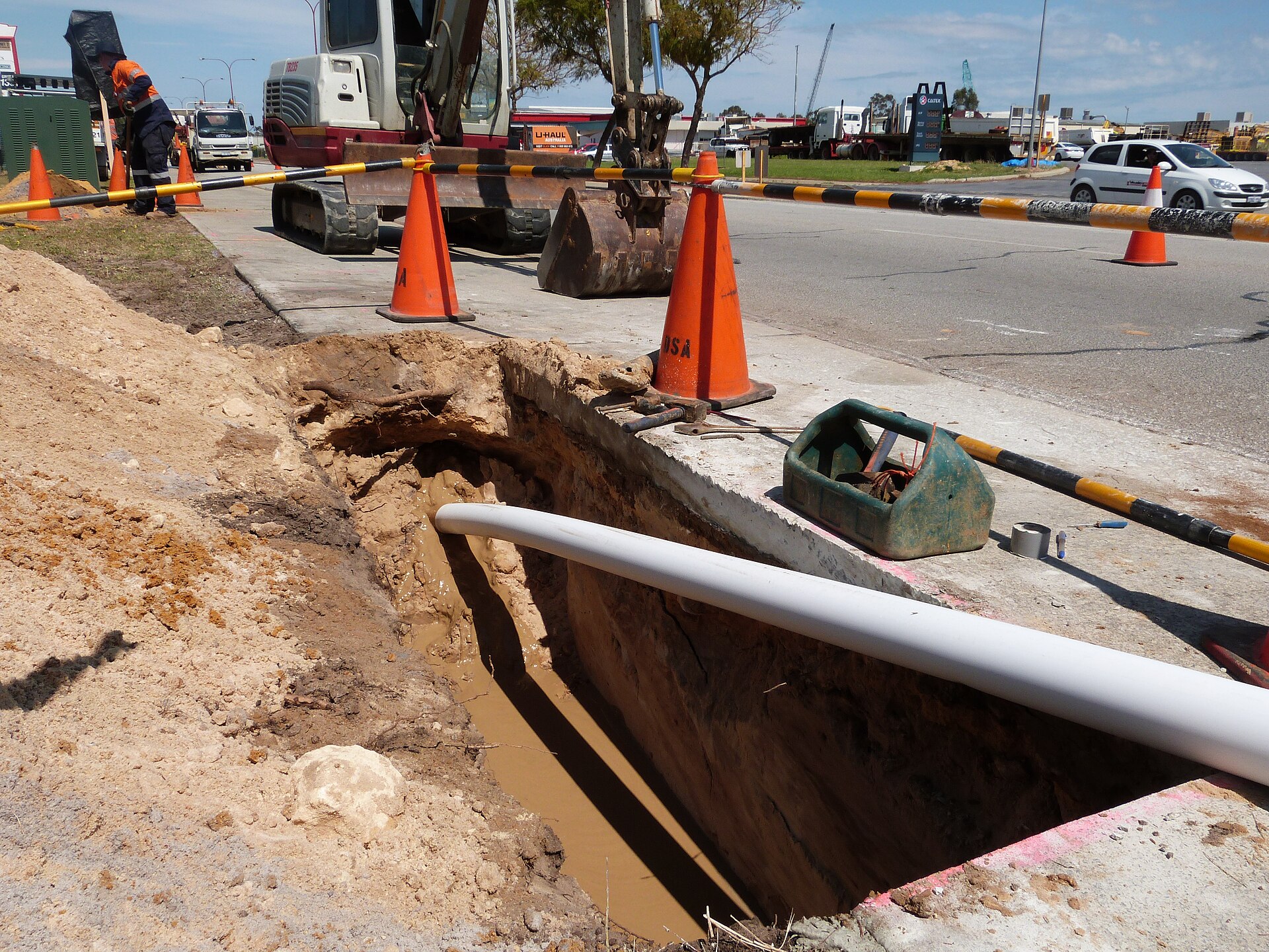 HDPE pipe being installed via directional drilling in excavated trench at underground utility construction site